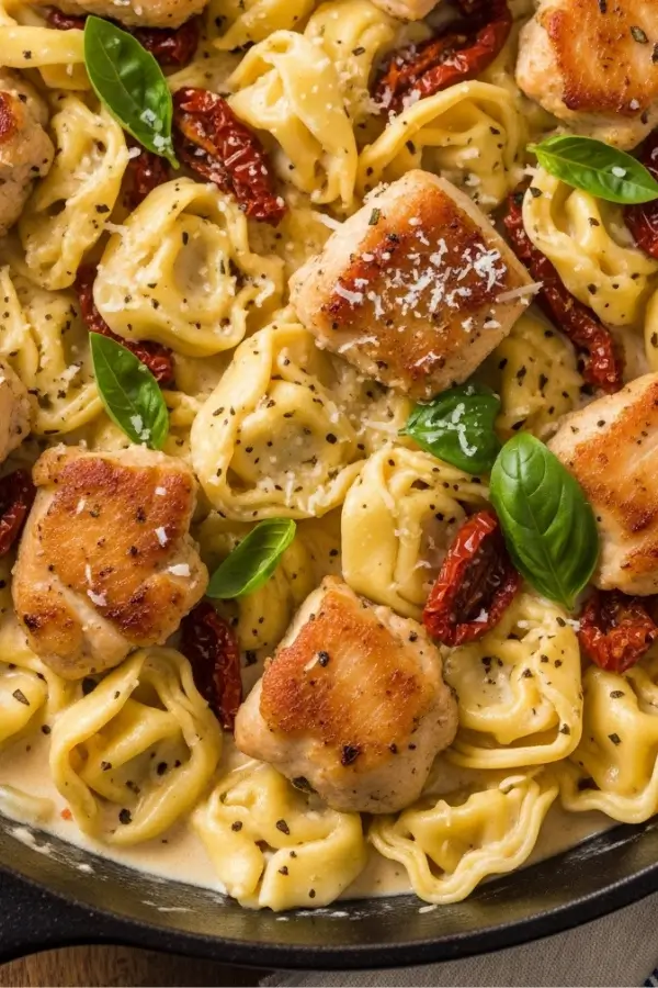Creamy skillet of cheese tortellini with golden chicken pieces , sundried tomatoes, Parmesan, and fresh basil in a rich garlic cream sauce