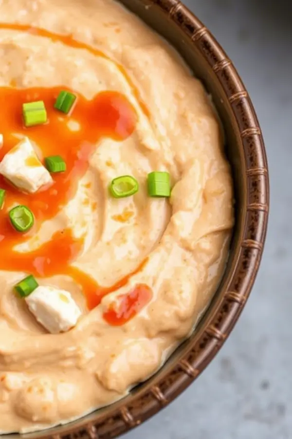 Creamy Buffalo Chicken Dip in a ceramic bowl topped with melted cheese, and chopped green onions