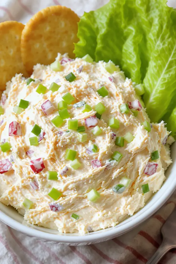 Creamy chicken salad with finely shredded chicken and minced celery, mixed in a smooth mayo base, served chilled in a white bowl with crackers and lettuce leaves on the side