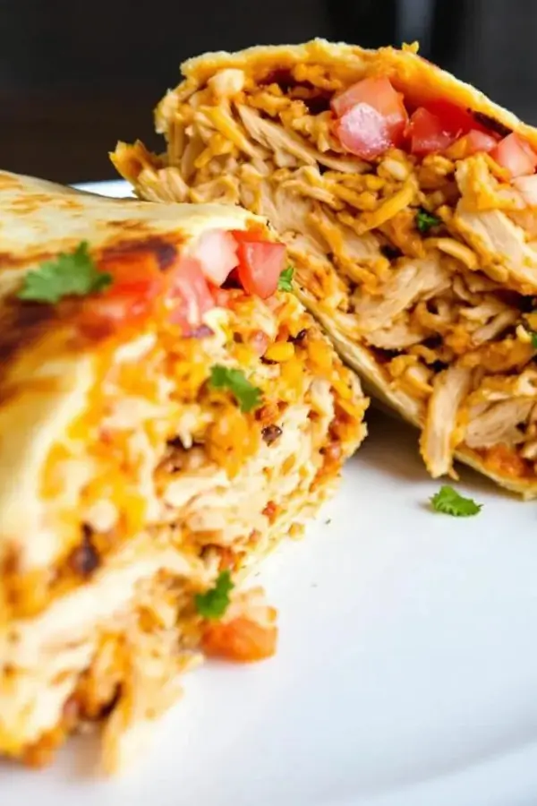 Toasted shredded chicken burrito sliced open, layers of juicy shredded chicken, seasoned rice, melted cheese, chipotle sauce, and fresh toppings like tomatoes and cilantro inside a golden, crispy tortilla on a plate
