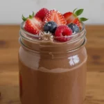 Creamy vegan chocolate mousse in a glass jar, topped with fresh berries and a dollop of coconut whipped cream on a table