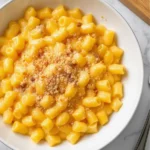 Creamy vegan mac and cheese in a bowl, golden cashew sauce coating tender macaroni, sprinkled with breadcrumbs on the modern kitchen countertop