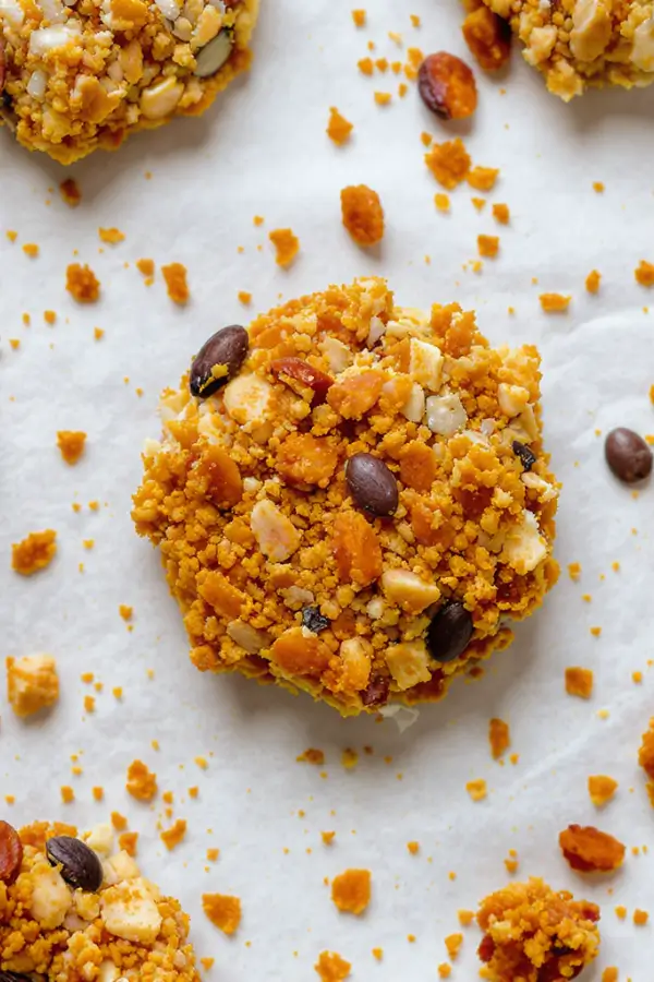 Top-down view of golden-brown keto granola clusters on a parchment-lined baking sheet, filled with nuts, seeds, and coconut flakes
