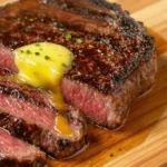 A perfectly seared ribeye steak with a golden-brown crust, sliced arranged on a wooden cutting board, drizzled with melted butter