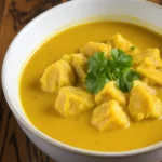 A bowl of creamy chicken curry with tender chicken pieces, and rich golden sauce, garnished with fresh cilantro, served on a table