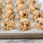 A tray of round no‑bake energy bites with chocolate chips and coconut on parchment on a modern kitchen countertop