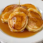 Small, golden-brown banana pancakes on a plate with maple syrup