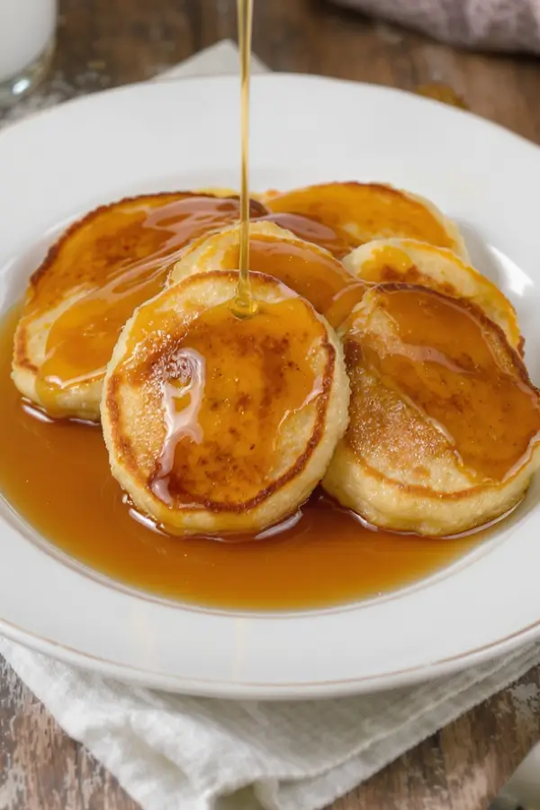 Small, golden-brown banana pancakes on a plate with maple syrup