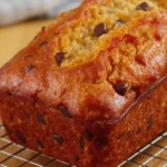 Golden, moist banana bread loaf studded with walnuts and dark chocolate chips, with a slightly cracked top, cooling on a wire rack