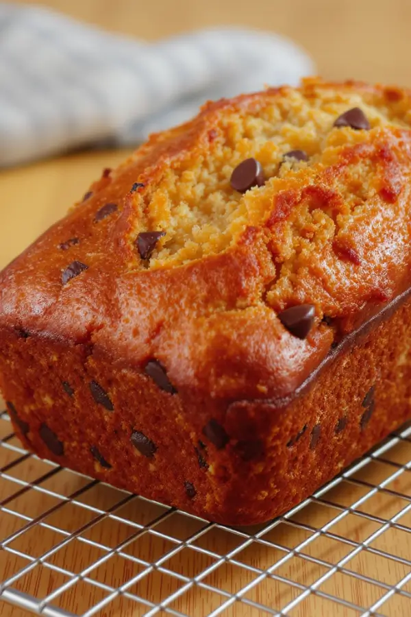 Golden, moist banana bread loaf studded with walnuts and dark chocolate chips, with a slightly cracked top, cooling on a wire rack