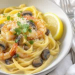 A bowl of creamy linguine pasta tossed with golden shrimp, sautéed mushrooms, and a rich lemon-garlic cream sauce, garnished with fresh parsley, lemon zest, and a sprinkle of Parmesan