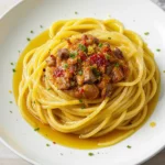 A plate of spaghetti glistening with anchovy-garlic olive oil sauce, speckled with red pepper flakes, lemon zest, and parsley, topped with a drizzle of olive oil