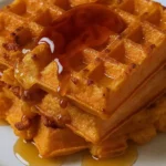 Golden sweet potato waffles stacked on a plate, topped with maple syrup