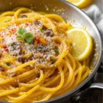 A skillet of spaghetti tossed in golden garlic butter sauce with melted anchovies, red pepper flakes, lemon zest, and parsley, topped with grated Parmesan and served with a twist of lemon