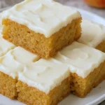 Golden apple cinnamon blondies topped with creamy maple cream cheese frosting, cut into neat squares on a small plate