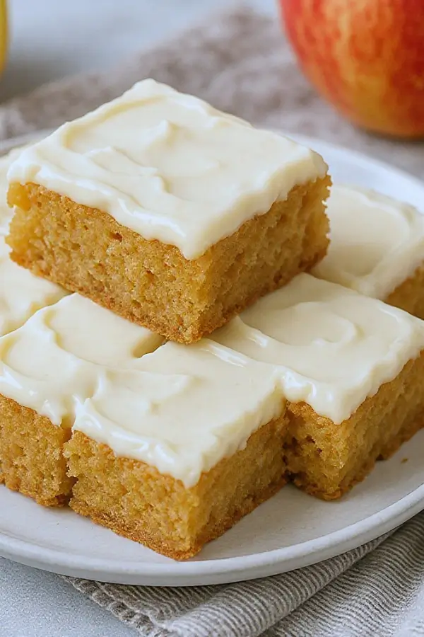 Golden apple cinnamon blondies topped with creamy maple cream cheese frosting, cut into neat squares on a small plate