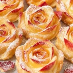 Golden puff pastry apple roses with red apple petals, dusted with powdered sugar and glazed with apricot jam on a table