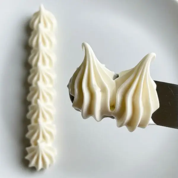 Spatula lifting icing with stiff peaks standing tall, test line piped on plate with clean edges