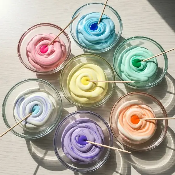 Several small bowls with white icing being tinted with gel food coloring using a toothpick