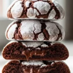 A stack of chocolate crinkle cookies on a white ceramic plate with one cookie broken in half