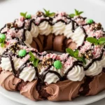 Chocolate pavlova wreath topped with fluffy peppermint whipped cream, dark chocolate drizzle, crushed peppermint candies, peppermint bark pieces, and fresh mint