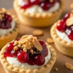 Mini golden-brown tart shells filled with creamy goat cheese, topped with glossy cranberry sauce and toasted almond crumble