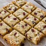 Cranberry white chocolate blondies cut into neat squares, cooling on parchment