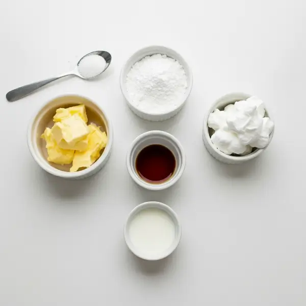 Softened butter, powdered sugar, marshmallow fluff, vanilla extract, salt, and a small splash of milk arranged neatly on a white kitchen countertop