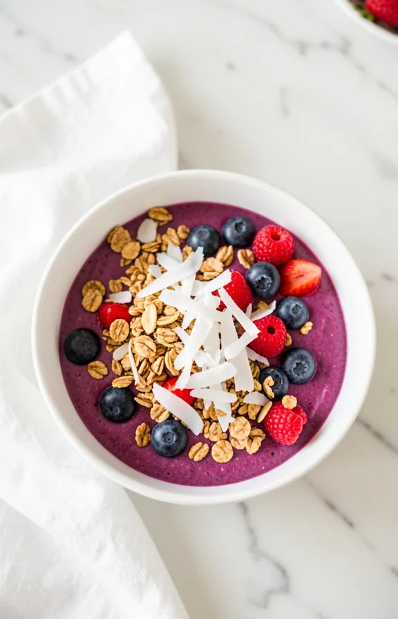 colorful berry smoothie bowl topped with granola and coconut on white ceramic bowl