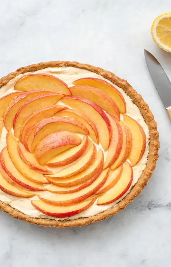 Fresh peach slices being arranged in overlapping concentric circles on a cream cheese filled tart shell before the apricot glaze is applied