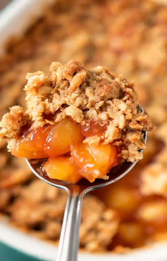 spoonful of golden peach crisp showing jammy peach filling and oat topping
