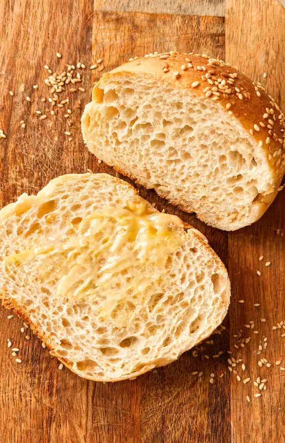 Soft sourdough discard hamburger bun split open on a worn wooden cutting board, the cut surfaces facing up to reveal a pillowy, golden-yellow crumb with a fine, even open texture
