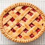 A whole golden-baked strawberry rhubarb lattice pie cooling on a wire rack