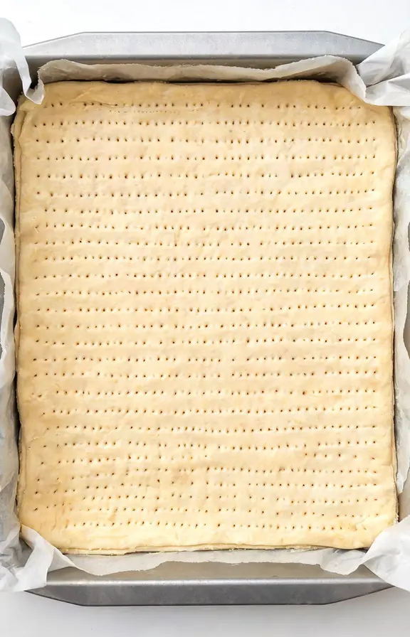 Blind baked puff pastry sheet with fork docking marks in a parchment lined baking pan before the apple filling is added