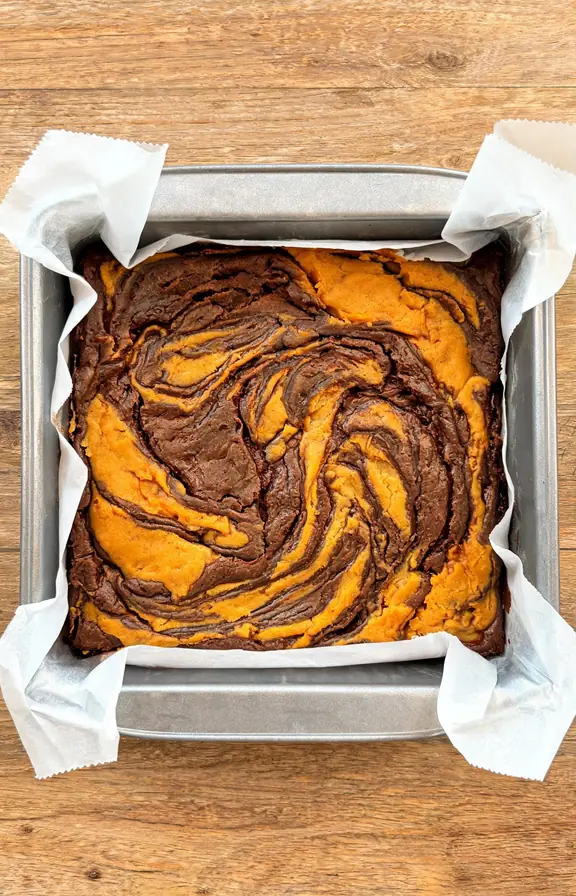 Chocolate pumpkin brownie batter swirled in a parchment lined baking pan before going into the oven
