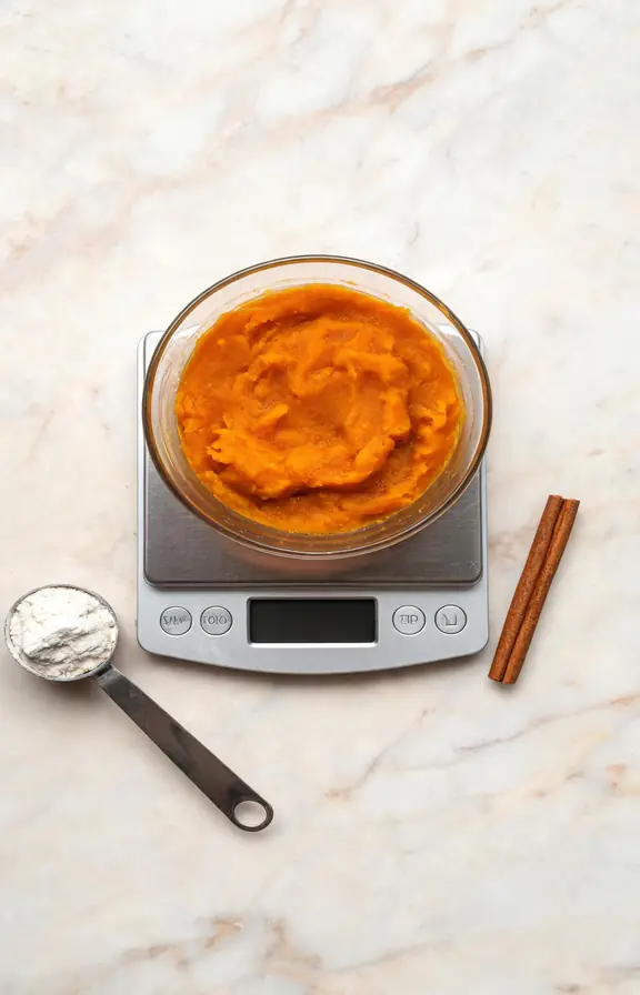 Kitchen scale weighing canned pumpkin puree in a glass bowl for gluten free muffins