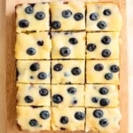 Lemon blueberry sheet cake in a half sheet pan, cut into squares, topped with lemon glaze and fresh blueberries