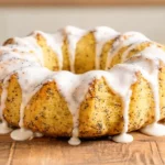 Whole lemon poppy seed bundt cake with white lemon glaze dripping down the sides on a wooden board