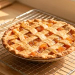 A whole baked peach pie with a golden lattice crust cooling on a wire rack