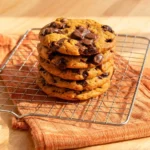 Stack of pumpkin chocolate chunk cookies with visible melted chocolate pools on a wire rack