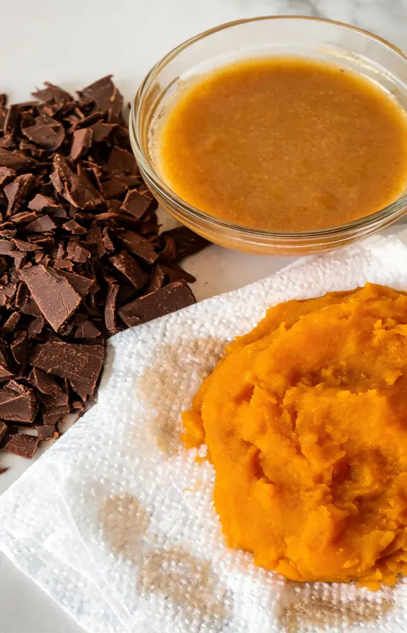Hand chopped chocolate chunks next to browned butter and blotted pumpkin puree on paper towels