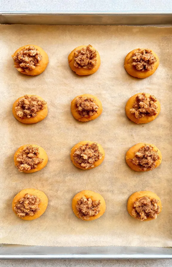 Overhead shot of pumpkin coffee cake cookie dough balls topped with cinnamon streusel on a parchment lined baking sheet before baking
