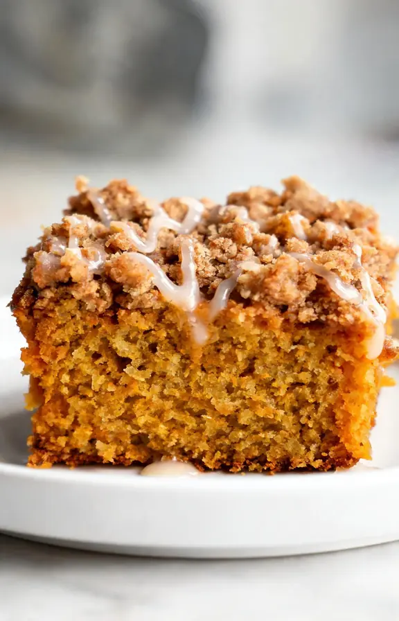 Close up of a single square of pumpkin coffee cake with visible cinnamon streusel crumbs and a drizzle of vanilla glaze