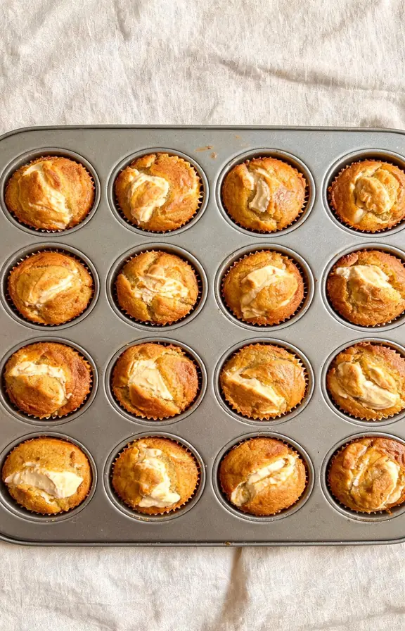 Overhead shot of pumpkin cream cheese muffins in a muffin tin, tops golden with a few cracked domes