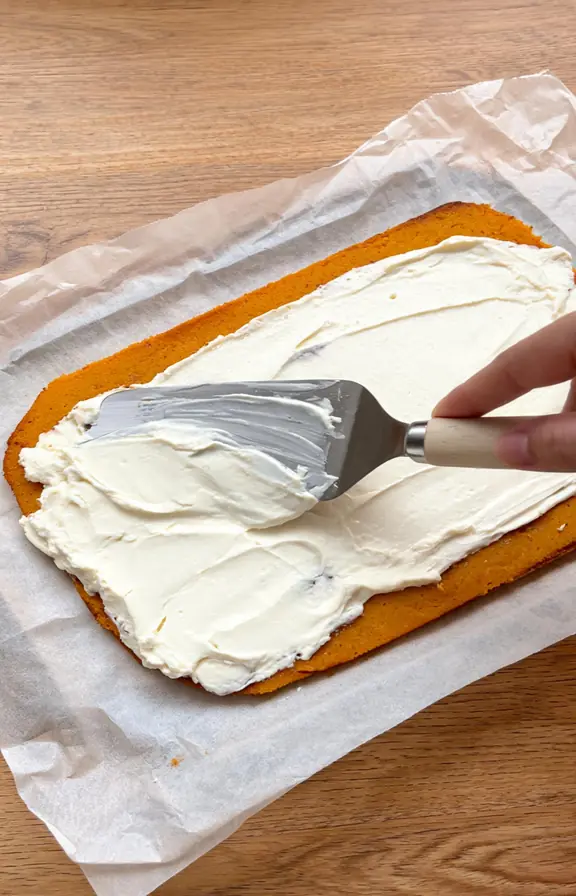 Warm spiced pumpkin cake being rolled inside parchment paper immediately after coming out of the oven
