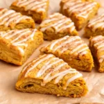 Tall golden pumpkin scones drizzled with cinnamon glaze, arranged on a parchment lined baking sheet