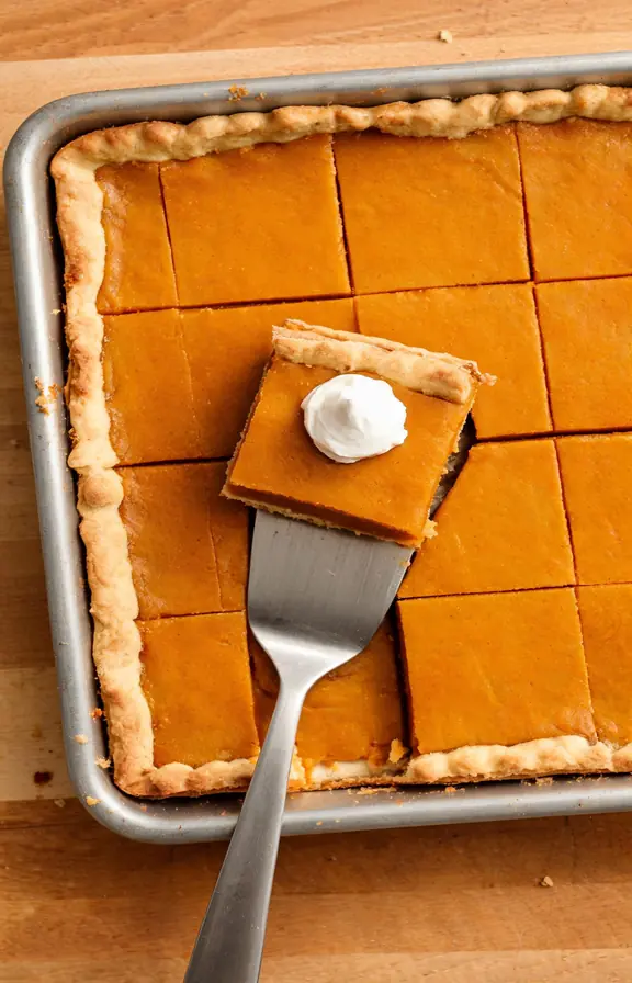 Pumpkin slab pie cut into squares on a sheet pan with a dollop of whipped cream on top