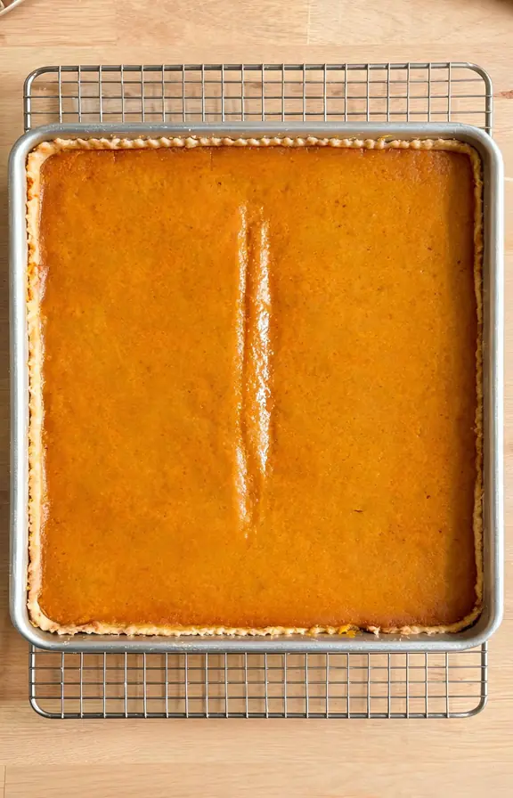Overhead shot of baked pumpkin slab pie in a sheet pan showing set edges and a slightly jiggly center strip