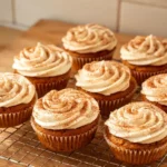 Pumpkin spice cupcakes with swirled cream cheese frosting and cinnamon dusting on a cooling rack