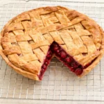 Whole raspberry pie with a golden lattice crust cooling on a wire rack